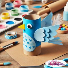 a blue bird made out of toilet paper sitting on top of a table next to paints