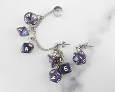 🎲 Carry your love of gaming with you wherever you go when you wear these mini FanRoll stardust galaxy swirl polyhedral dice chained ear cuffs! All seven polyhedral dice are present on the chain and dangling from the posts. These are the perfect fancy and funky accessory for game night, cons, or wherever you feel like showing off your love of gaming and dice. This is a mismatched set with a cuff designed for the right ear (but can be worn on the left as well) with six dice and a post for the oth Dnd Jewelry, Geek Aesthetic, Dice Jewelry, Weird Earrings, Dnd Crafts, Ear Cuff Chain, Adopt Idea, Aesthetic Earrings, Jewelry Ear