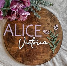 a wooden sign that says alice victoria next to some flowers on a white cloth background