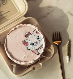 a cake in a box with a cat face on it and a fork next to it