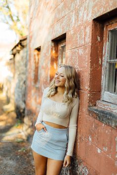 a woman leaning against the side of a brick building with her hands on her hips