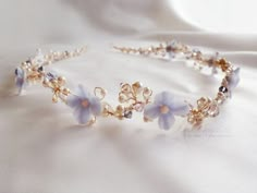 a white and blue flower headband with pearls on it's side, sitting on a bed