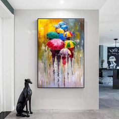 a black dog sitting in front of a painting with umbrellas on it's back