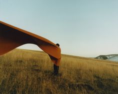 a person standing in the middle of a field with an orange blanket over their head