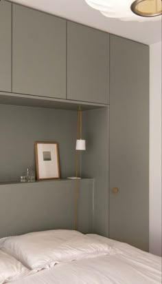 a bed with white sheets and pillows in a room that has gray cabinets on the wall