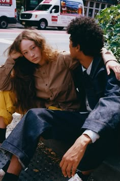 a young man and woman sitting on the curb