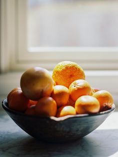 a bowl full of oranges and lemons on a table next to a window