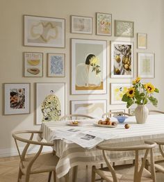 a dining room table with chairs and pictures on the wall above it, along with vases filled with sunflowers