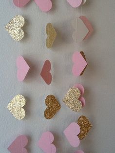 some pink and gold hearts hanging from a string on a white wall in the shape of hearts