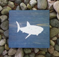 a wooden sign with a shark painted on it sitting next to some rocks and grass