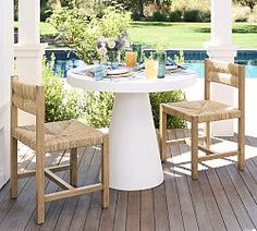 an outdoor table and chairs on a deck next to a pool with water in the background