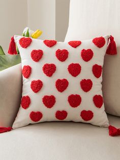 a red and white pillow with hearts on it sitting on a couch next to a potted plant