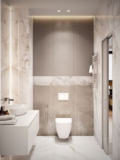 a white toilet sitting next to a bathroom sink under a mirror in a room with marble walls