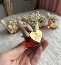 someone holding a jar with flowers in it on a white blanket next to other small vases