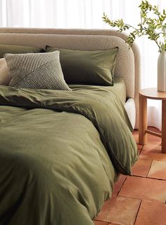 a bed with green sheets and pillows on top of it next to a small table