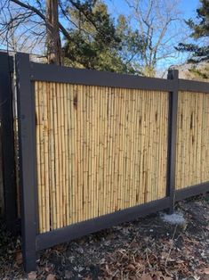 a fence made out of bamboo sticks in front of some trees and bushes with no leaves on the ground