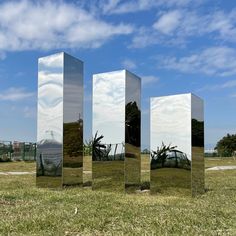 three mirrored cubes sitting on top of a grass covered field under a blue sky