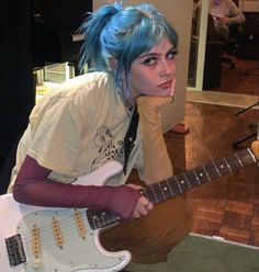 a woman with blue hair is holding a guitar and posing for the camera in front of her