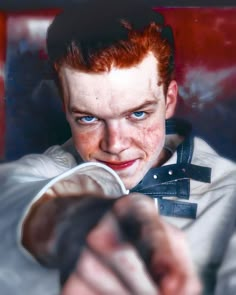 a young man with red hair and blue eyes pointing at the camera