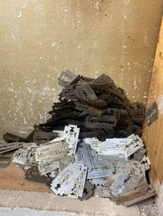 a pile of broken pieces of wood sitting on the ground next to a wall with peeling paint