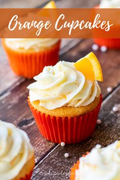 orange cupcakes with white frosting and an orange slice on top sitting on a wooden table