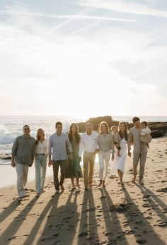 a group of people standing on top of a sandy beach next to the ocean at sunset