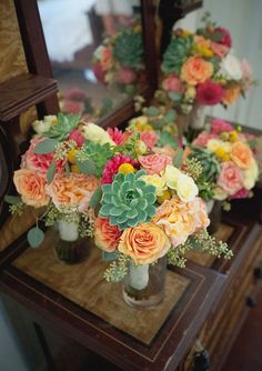 there are many flowers in vases on the table next to each other and a mirror behind them