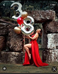 a woman in a red dress is holding balloons and the number three on her chest