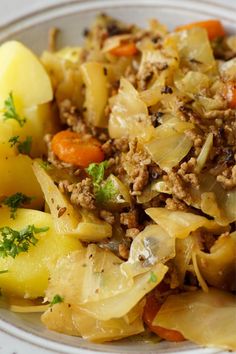 a white plate topped with cabbage and meat next to potatoes, carrots and parsley