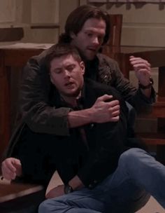 two men are sitting on the floor and one is holding his arm around the other