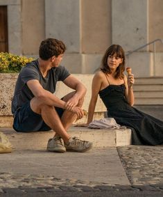 a young man and woman sitting on the ground eating ice cream while looking at each other