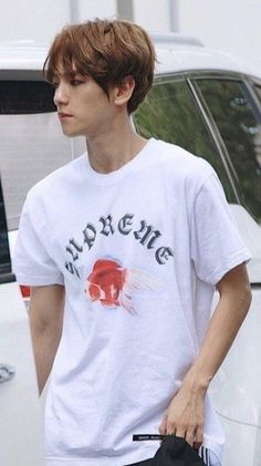 a young man holding a skateboard next to a white car and another person in the background