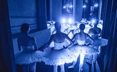 four ballerinas in white tutus are lined up with their skirts down and lights on behind them