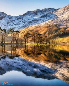 the mountains are covered in snow and reflecting on the still water, as well as trees