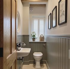 a white toilet sitting under a window next to a sink and a wooden framed mirror