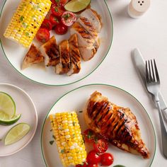 two plates with grilled chicken and corn on the cob next to lime wedges