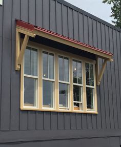 a gray building with two windows and a red roof on the top window sill