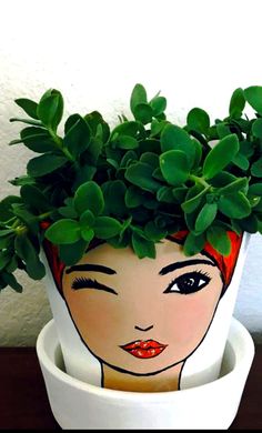 a potted plant with a woman's face painted on the side and green leaves growing out of it