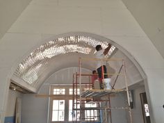 two men on scaffolding work on the ceiling in a large room that is under construction