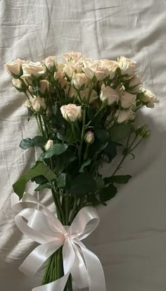 a bouquet of white roses tied in a ribbon on a bed sheet with a bow