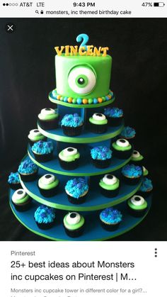 a three tiered blue and green cake with cupcakes in front of it