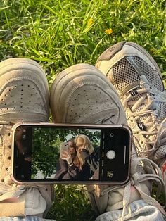 someone taking a selfie with their cell phone while sitting on the ground in front of some grass