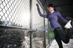 a woman is leaning against a fence and stretching