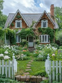 a house that is surrounded by flowers and greenery in the front yard with a white picket fence