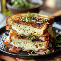 two grilled sandwiches stacked on top of each other in a black plate with green sprouts