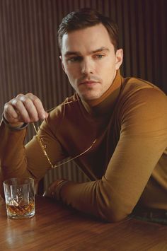 a man sitting at a wooden table with a glass in front of him and his hand resting on the edge