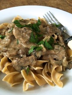 a white plate topped with pasta covered in gravy next to a knife and fork