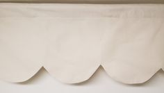 a white bed skirt with scalloped edges hanging on a wall