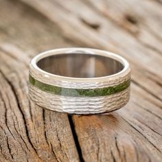 a wedding band that has been made with silver and green enamel inlays, on top of a wooden surface