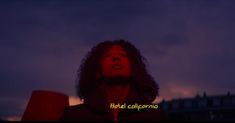 a woman with curly hair standing in front of a dark sky at night, looking up to the sky